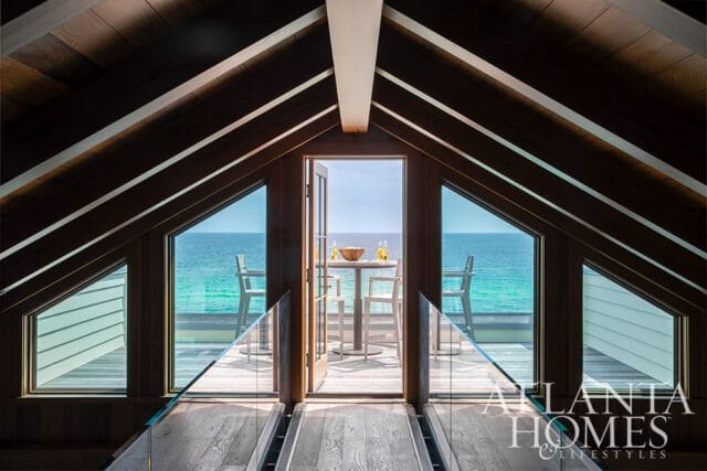 Wooden walkway with glass railings leading to open doors with ocean view, table and chairs on deck