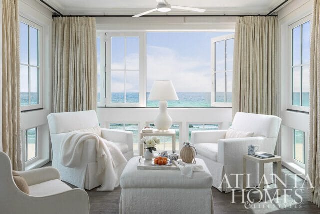 Seaside primary bedroom seating area with white slipcovered chairs and ottoman overlooking the