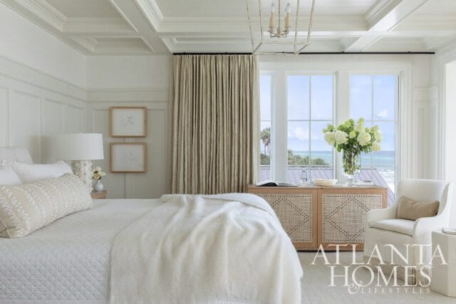Primary bedroom with coffered ceiling, white bedding, and ocean view through large windows.
