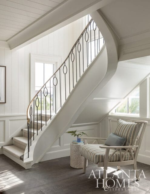 Curved staircase with black railing, carpeted stairs, and striped armchair.