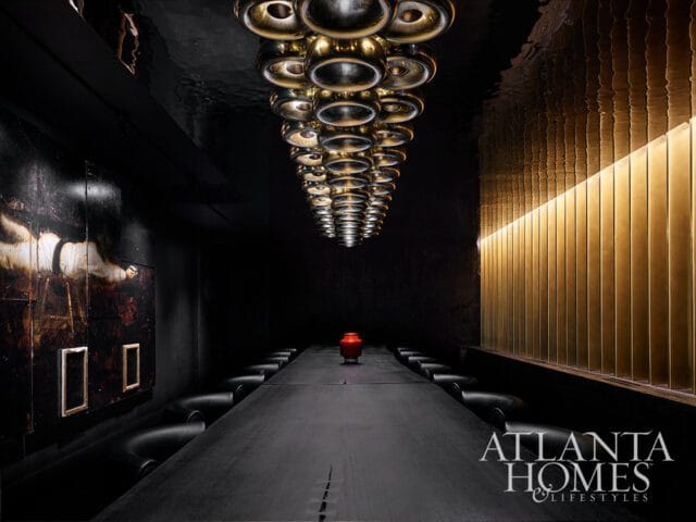 Dark dining room with long table, black chairs, and brass wall panels.