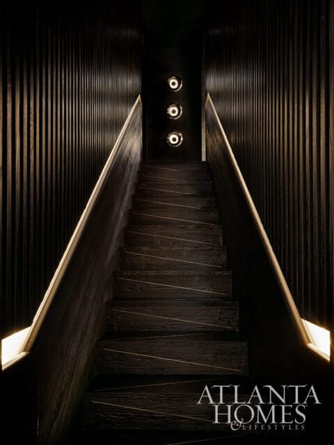 Dark wood staircase with illuminated handrails and three wall sconces
