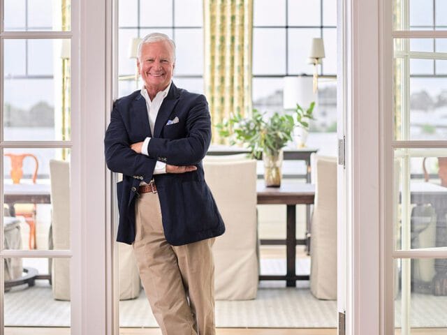 Man in navy blazer and tan pants with arms crossed, smiling.