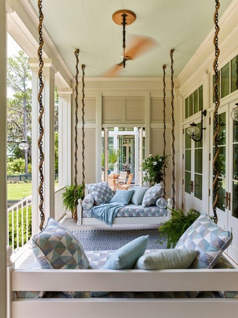 Porch swing with blue geometric cushions and pillows, rug, and ceiling fan.