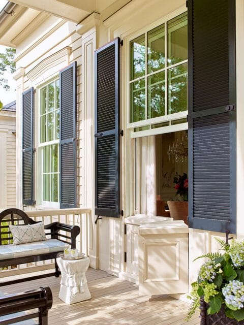 Cream-colored house with black shutters and a dark wood bench on the porch.