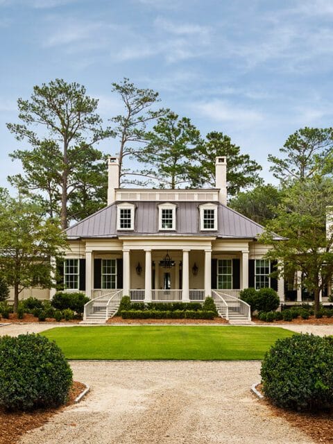 Southern plantation-style home with white columns, gray metal roof, and manicured lawn.