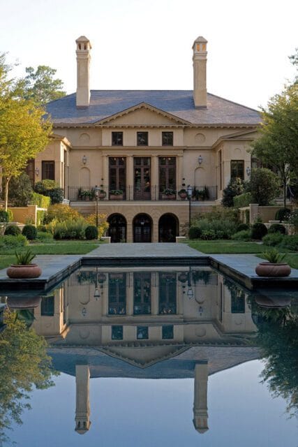 Large tan mansion with arched doorways and symmetrical windows reflected in a still pool.