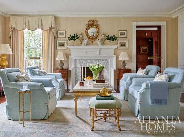 Living room with light blue upholstered chairs, marble fireplace, and gold accents.