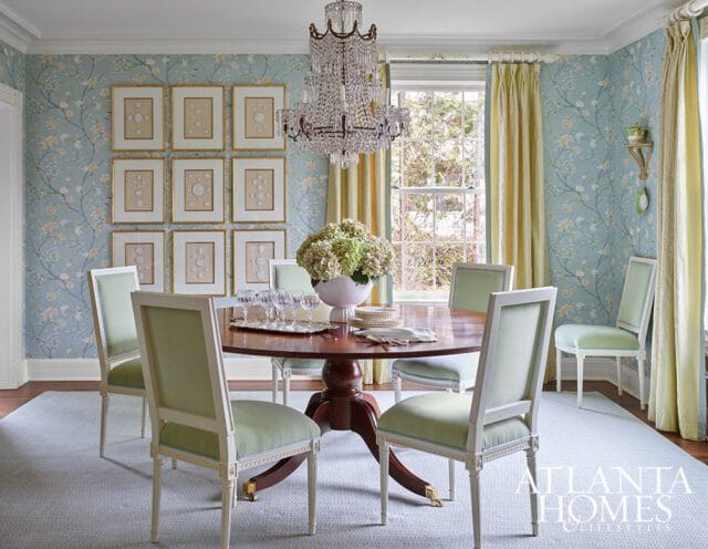 Dining room with floral wallpaper, crystal chandelier, and light green upholstered chairs.
