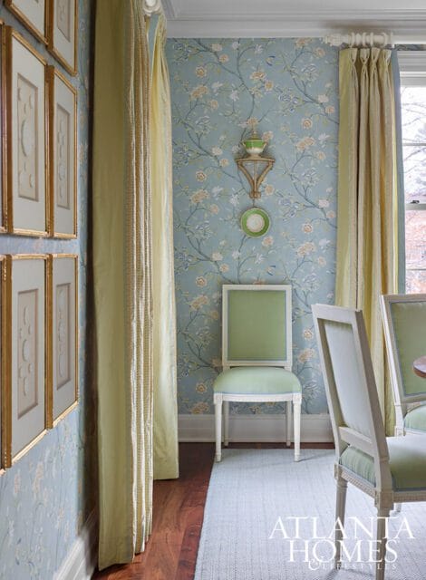 Dining room with floral wallpaper, green upholstered chairs, and gold framed art.