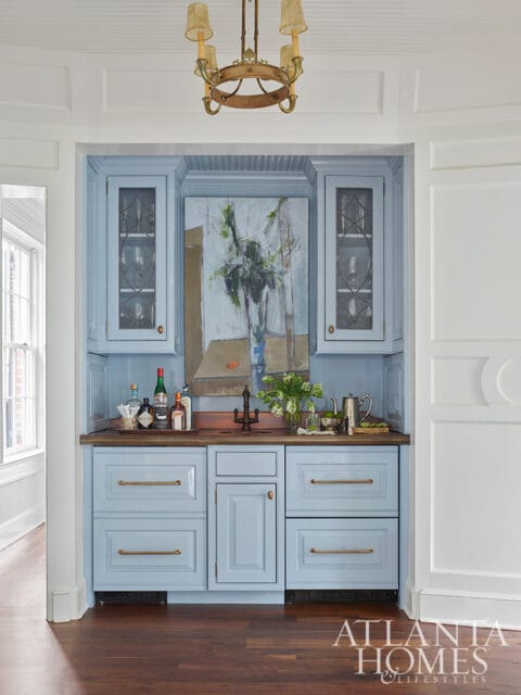 Light blue bar cabinet with glass doors, wood countertop, and abstract painting.