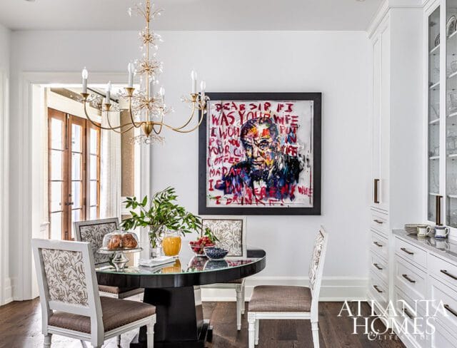 Dining area with abstract portrait, round table, and white cabinetry.