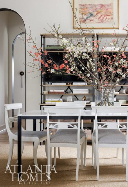 Dining room with white chairs, marble table, and shelves with books and flowers.