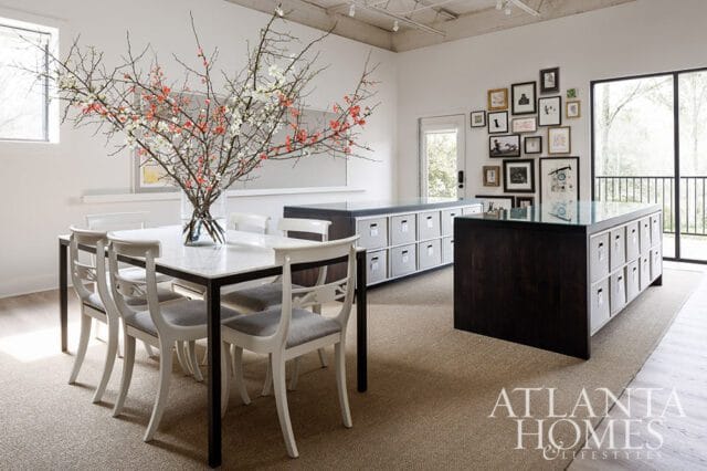 Dining area with marble table, white chairs, and storage island. Gallery wall on white wall.