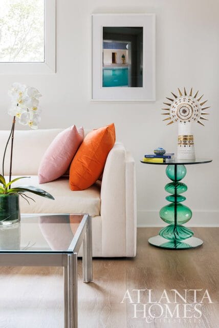 Cream sofa with pink and orange pillows, glass coffee table, and green sculptural side table.