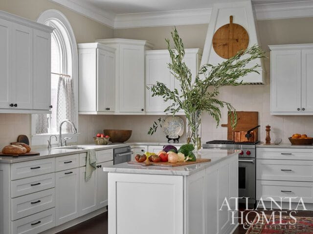 White kitchen with marble island, stainless steel appliances, and arched window.