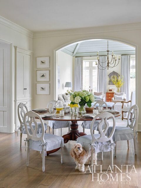 Dining room with round wooden table, upholstered chairs, and dog.