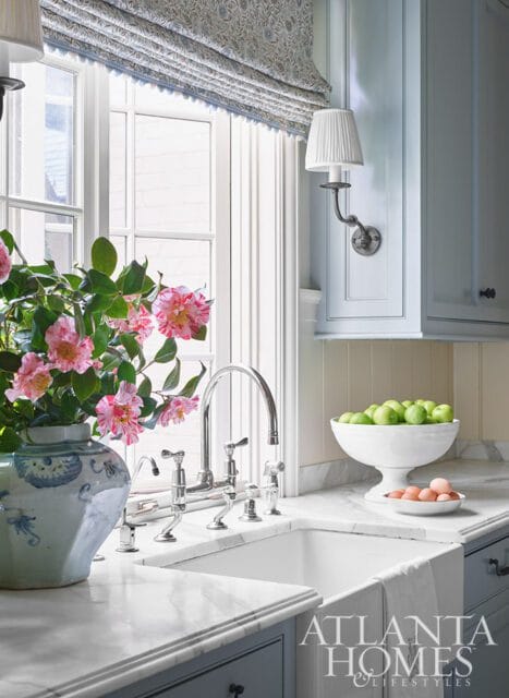 Farmhouse sink with chrome faucet, marble counters, and floral arrangement.