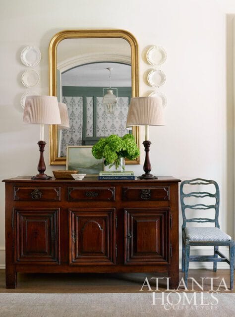 Dark wood buffet with gold mirror, two lamps, and green hydrangeas.