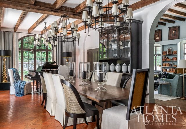 Dining room with wood beam ceiling, large chandelier, dining table, chairs, and grand piano