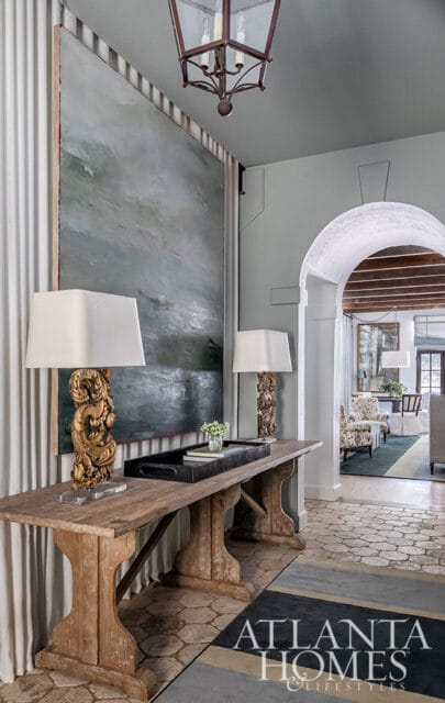 Hallway with large abstract painting, ornate gold lamps on wooden console table, and arched doorway