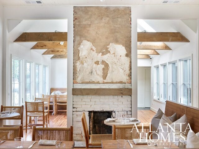 Dining room with wicker chairs, wooden tables, and a brick fireplace with exposed plaster