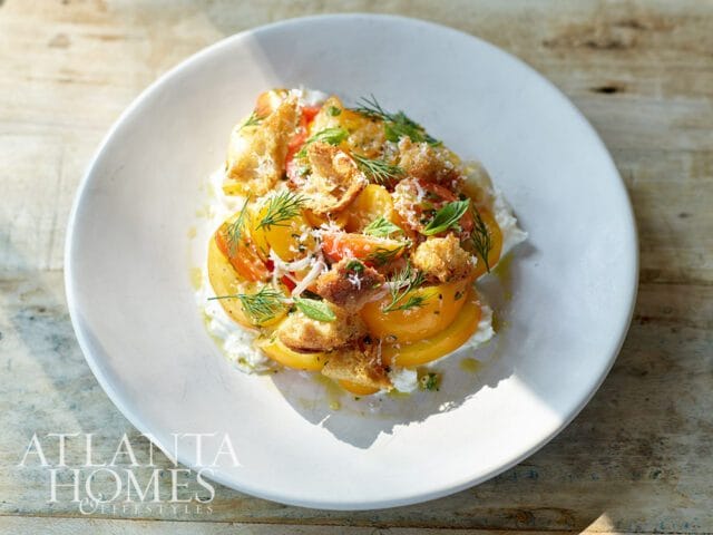 Yellow tomato salad with cheese, croutons, and dill on a white plate