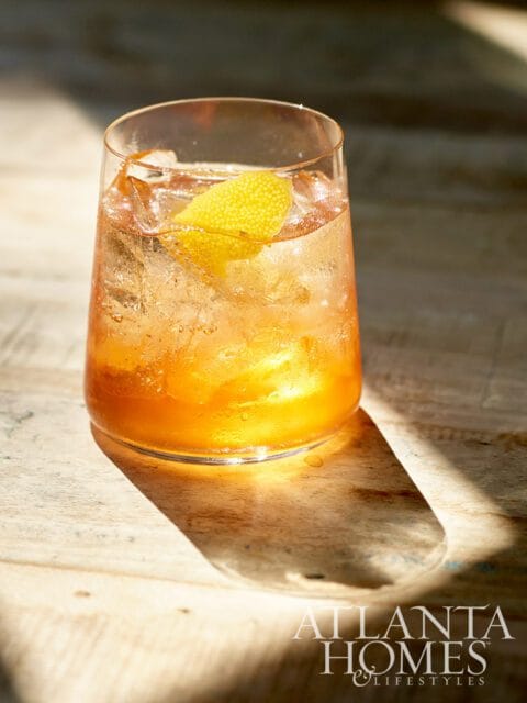 Cocktail with ice and lemon peel in a glass, with Atlanta Homes & Lifestyles logo