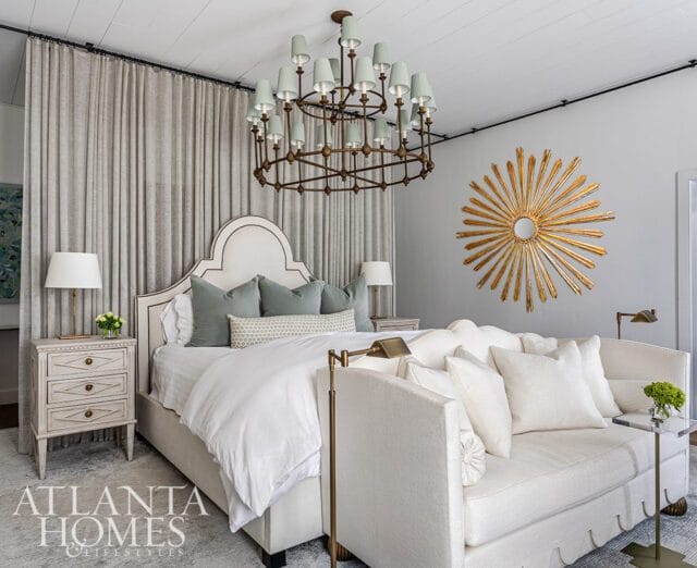 Bedroom with tufted headboard, sage green pillows, white bedding, and a sunburst mirror.