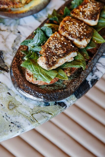 Three pieces of grilled fish with sesame seeds on spinach and toast
