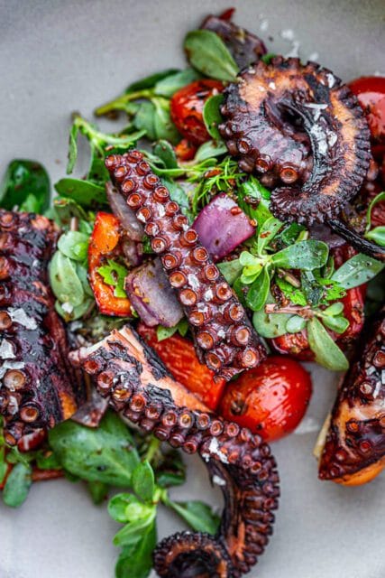 Grilled octopus tentacles with cherry tomatoes and greens