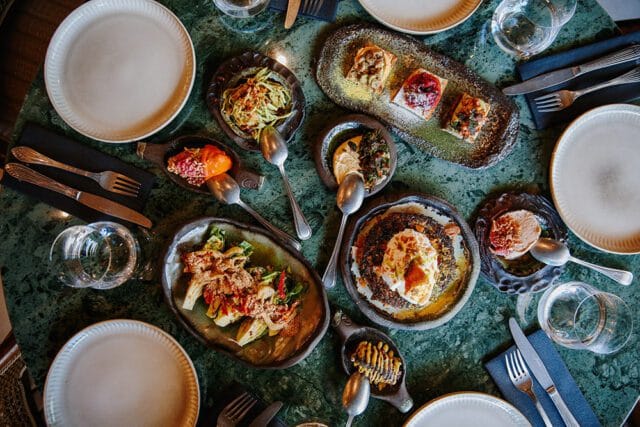 Table with multiple small plates of food, including appetizers and entrees, set on a green marble
