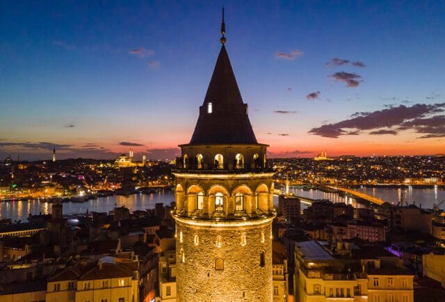 Galata Tower at dusk with city lights and a bridge over water