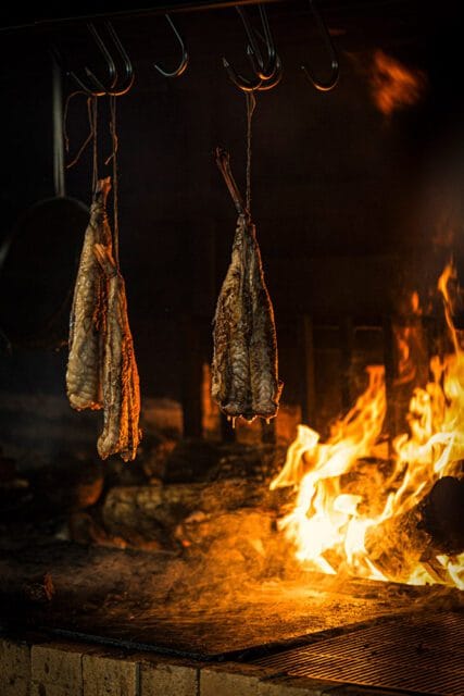 Two whole fish hanging over a fire, being smoked or cooked.
