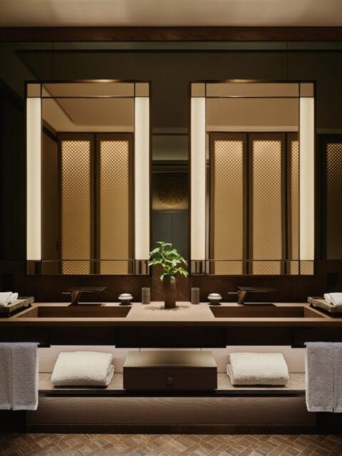 Bathroom with double vanity, wood accents, and backlit mirrors.
