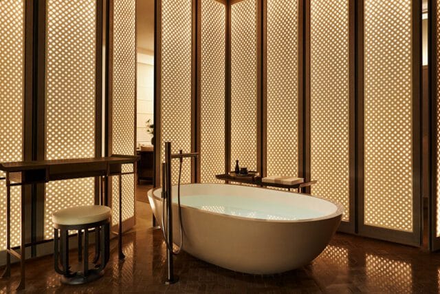 Bathroom with freestanding tub, wood floors, and illuminated lattice screens.