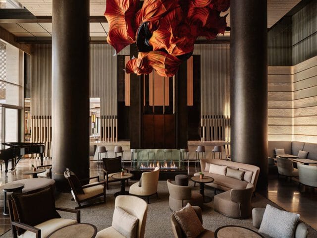 Lounge with fireplace, grand piano, and seating areas. Orange sculptural art hangs overhead.