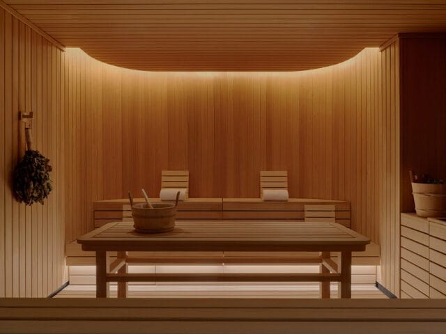 Wooden sauna with tiered benches, bucket, and whisk. Warm ambient lighting.
