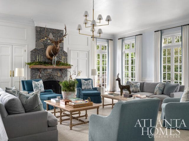 Living room with stone fireplace, mounted elk head, teal and gray sofas, and Atlanta Homes &