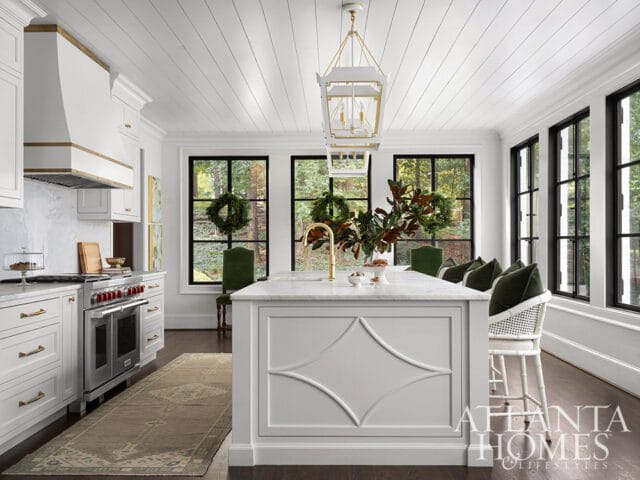 White kitchen with marble island, brass faucet, and stainless steel range.