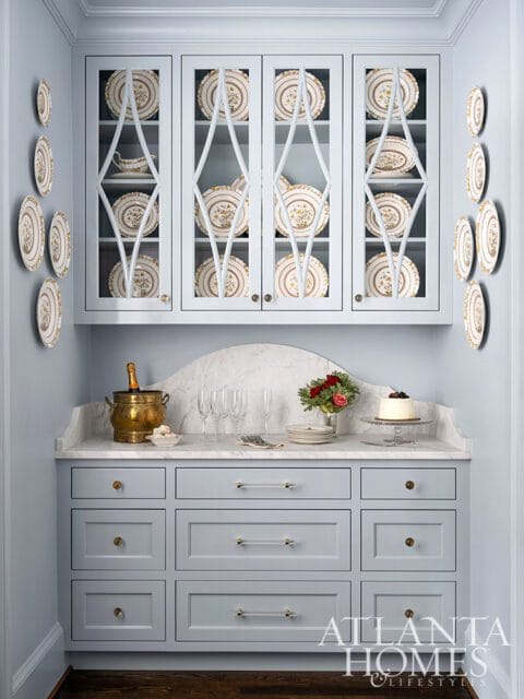 Light blue butler's pantry with glass-front cabinets displaying china and a marble countertop with