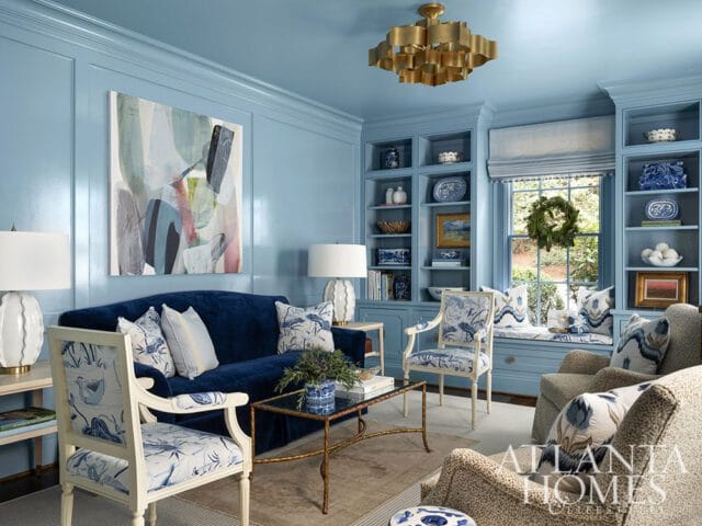 Blue living room with navy sofa, patterned chairs, built-in bookshelves, and abstract art.