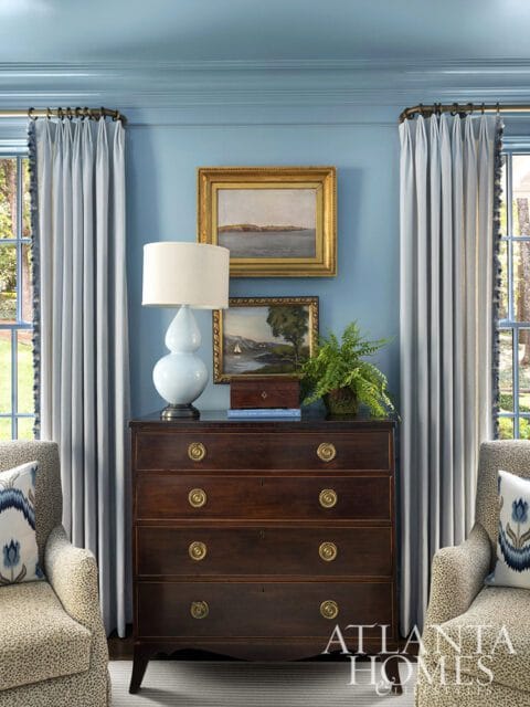 Blue room with dark wood dresser, light blue lamp, two armchairs, and pale blue curtains.