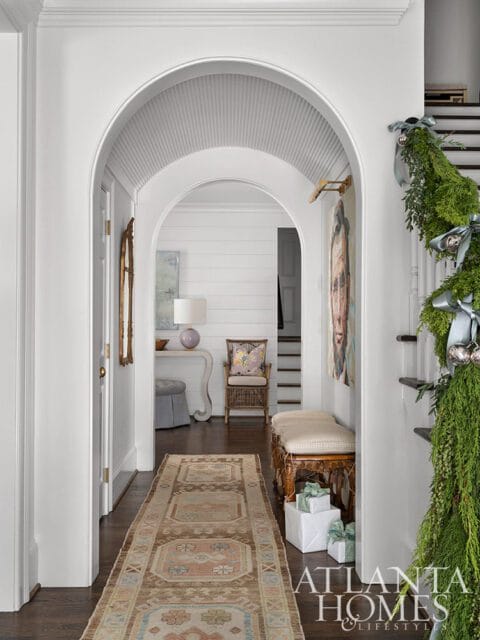 Hallway with arched doorways, runner rug, bench, and Christmas garland on stairs.