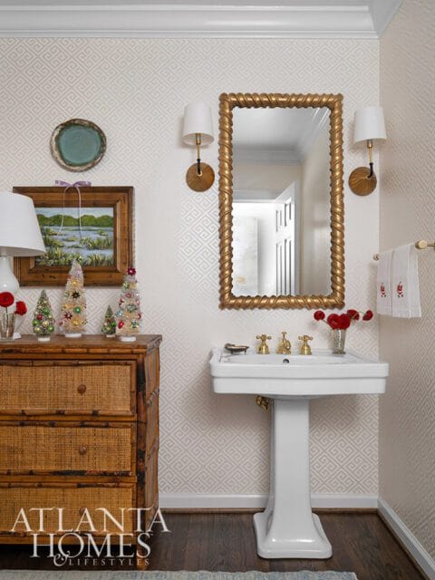 Powder room with white pedestal sink, gold mirror, and bamboo dresser.