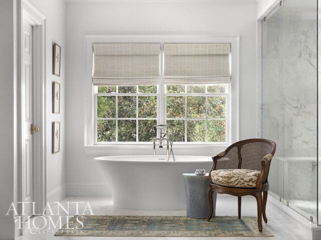White bathroom with freestanding tub, cane chair, marble shower, and Atlanta Homes logo