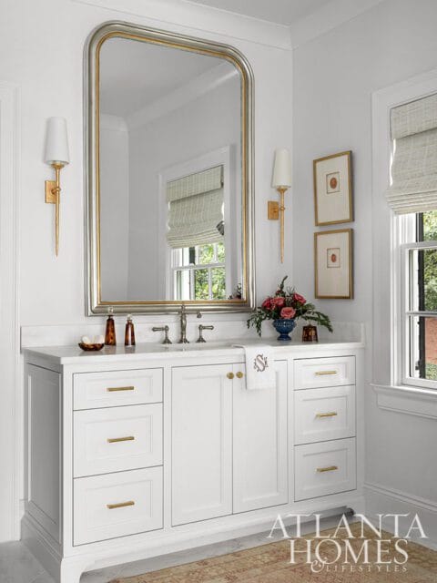 White bathroom vanity with marble countertop, gold hardware, and large arched mirror.