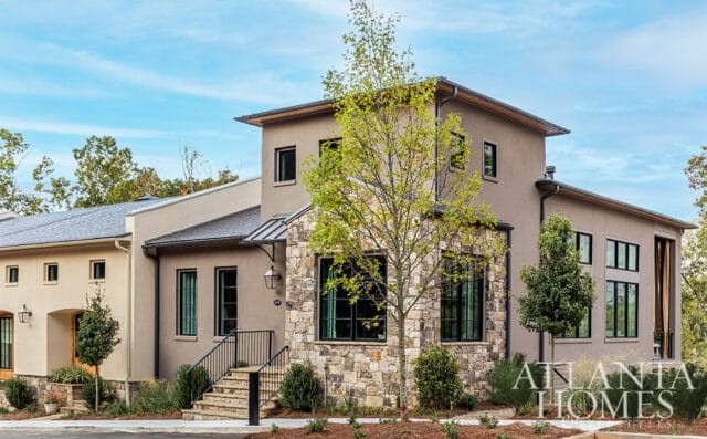 Modern home with stucco and stone facade, dark windows, and metal roof.