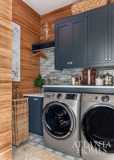 Laundry room with wood-paneled walls, gray subway tile backsplash, and navy cabinets. Features two