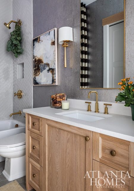 Bathroom with light wood vanity, white quartz countertop, brass fixtures, and abstract art.